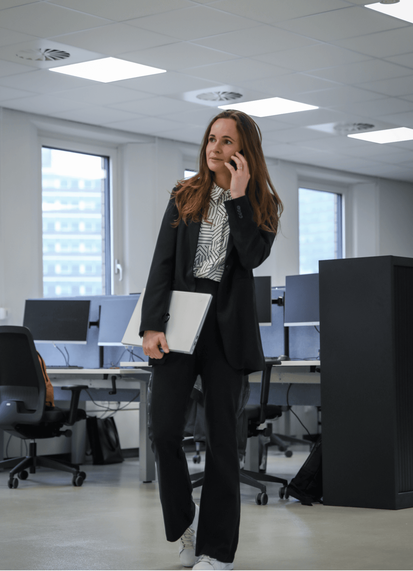 Werknemer staat met een laptop onder haar arm en is aan het bellen.